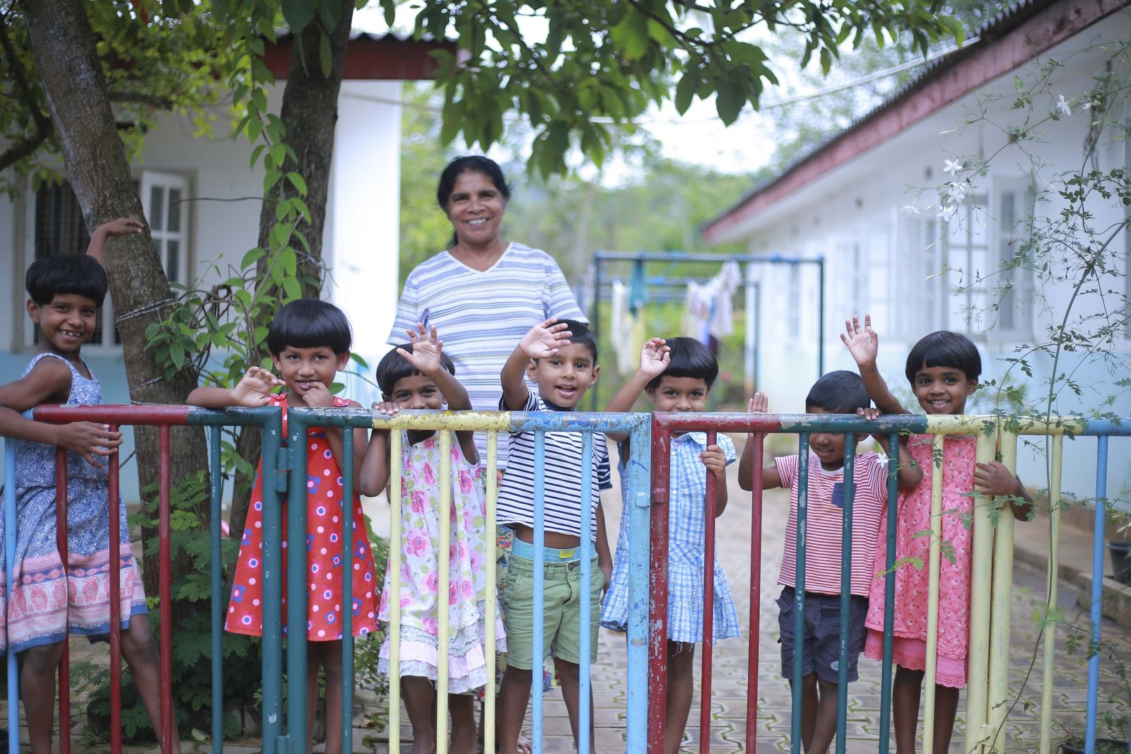 Jonge kinderen van Home of Hope zwaaien bij het hek, met een begeleider daarachter