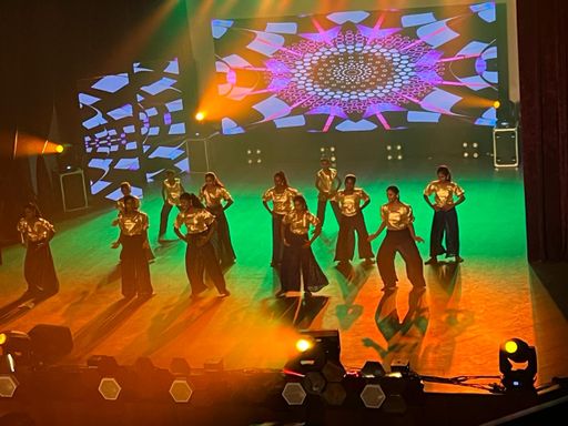 Dansgroep in gouden tops op een verlicht podium tijdens een optreden